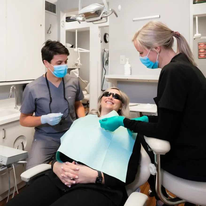A patient smiling with two dental team members beside her treatment chair